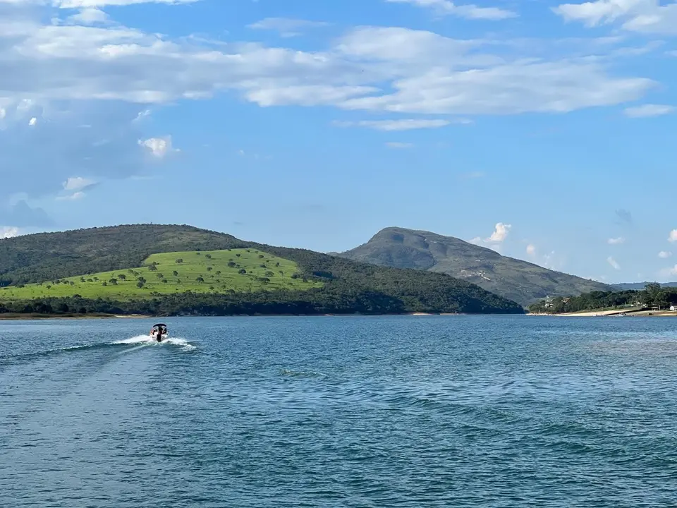 Lancha cruzando a represa de Furnas com morros verdes ao fundo